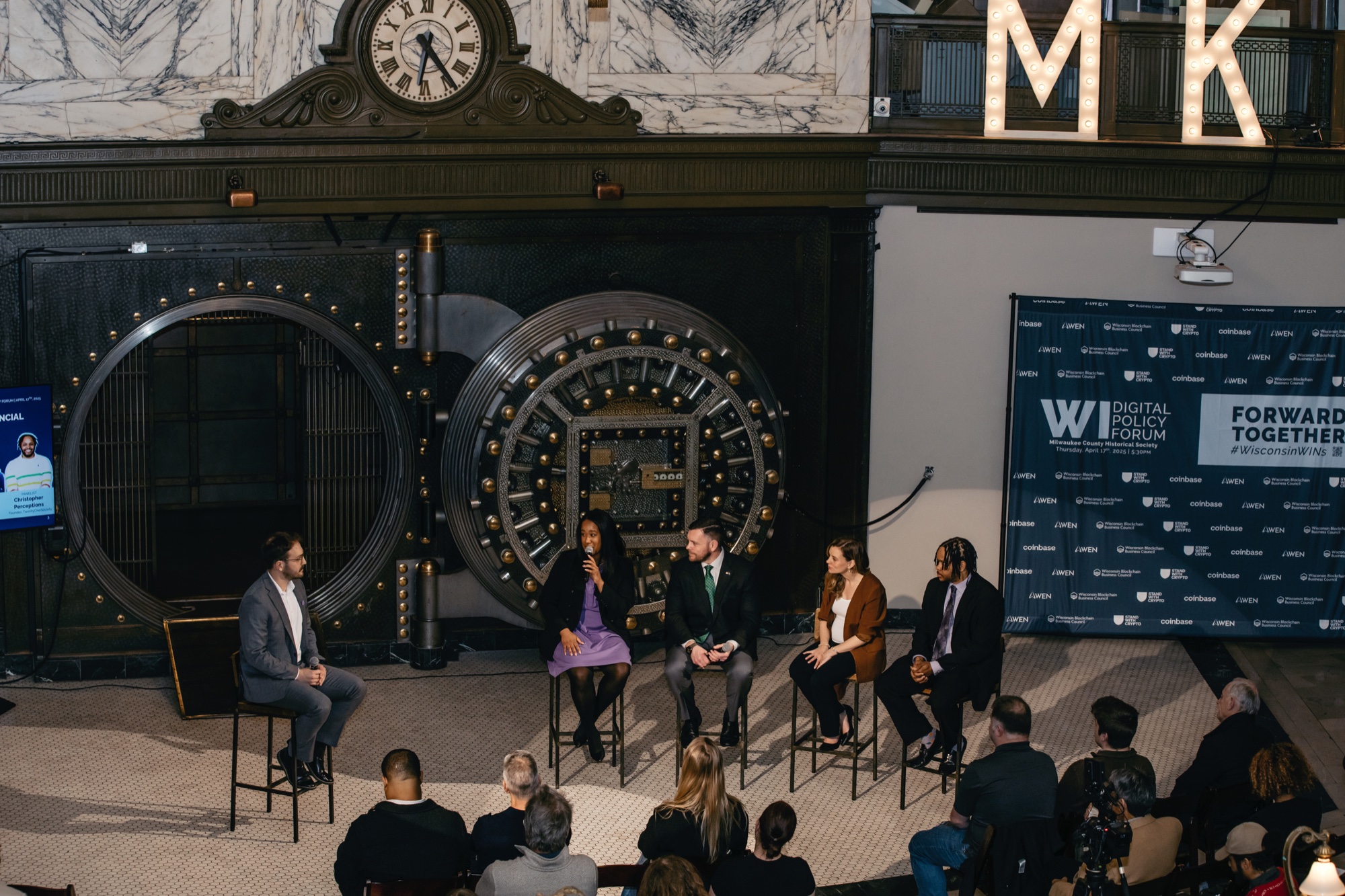 Wisconsin Digital Policy Forum panel on stage in front of the bank vault and branded ‘Forward Together’ backdrop